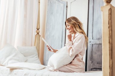 Genç kadın evde yatakta dijital tablet kullanarak yan görünüm
