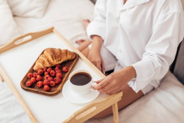 kadın kahvaltı kahve, kruvasan ve ahududu ile evde yatakta görüntü kırpılmış