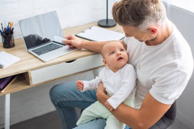 kredi kartı online alışveriş ve holding bebek kızı evde bilgisayar masa başında oturan babası