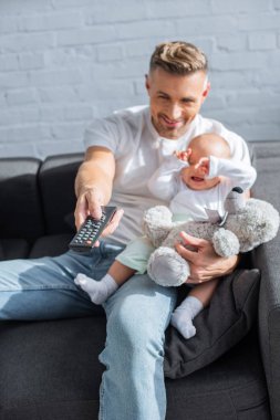 Bebek kızıyla kanepede oturan, uzaktan kumanda holding ve evde televizyon izlerken baba gülümseyerek