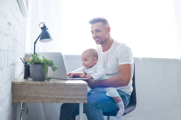 Sorrindo Pai Sentado Cadeira Segurando Bebê Usando Laptop Casa — Fotografia de Stock