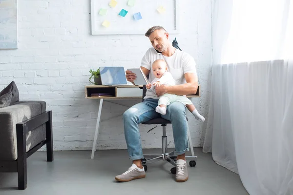 Vader Zittend Een Stoel Laptop Kijken Schattige Baby Dochter Houden — Stockfoto