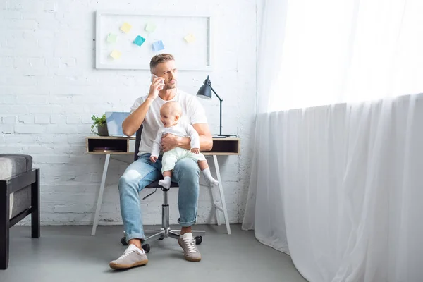Πατέρας Κάθεται Καρέκλα Μιλώντας Στο Smartphone Και Κρατώντας Μωρό Κόρη — Δωρεάν Φωτογραφία