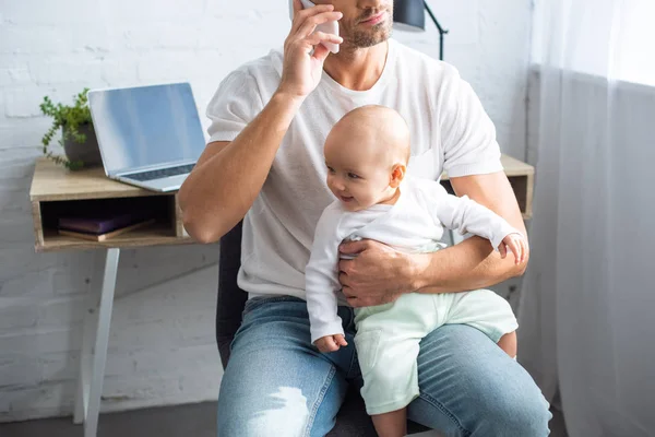 Cropped View Father Sitting Chair Talking Smartphone Holding Smiling Baby — Free Stock Photo