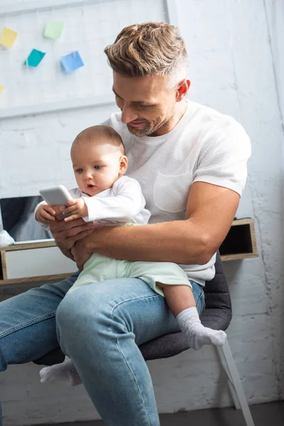 Smiling Father Sitting Chair Holding Adorable Baby Daughter Using Smartphone — Stock Photo, Image