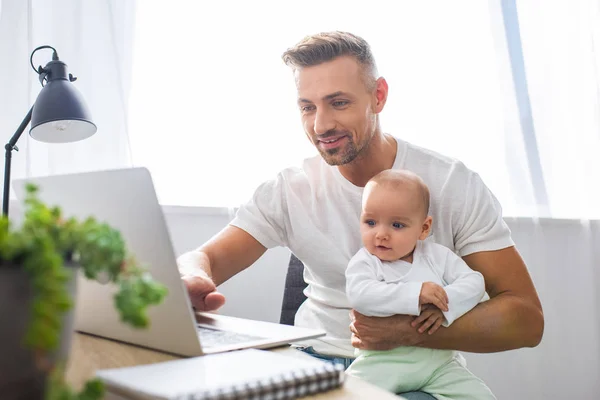 Leende Far Sitter Vid Dator Skrivbord Hemma Och Håller Baby — Stockfoto