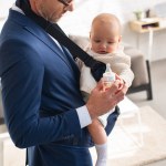 Businessman in suit holding bottle and infant daughter in baby carrier