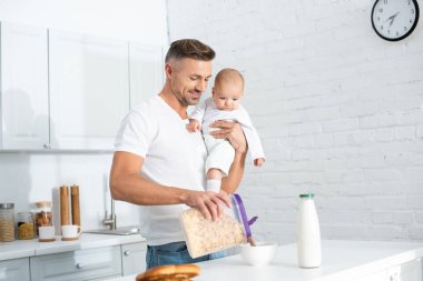 Bebek kızı tutarak ve beyaz mutfakta kahvaltı hazırlarken baba