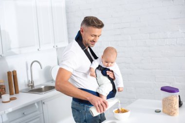 baba bebek taşıyıcı bebek kızı tutan ve bir kase mısır gevreği süt dökme 