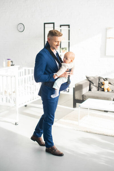 весёлый бизнесмен держит в комнате новорожденную дочь с солнечным светом

