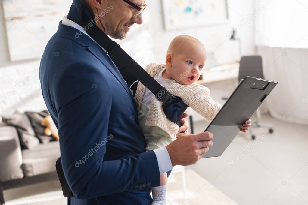businessman in suit holding clipboard and infant daughter in baby carrier 