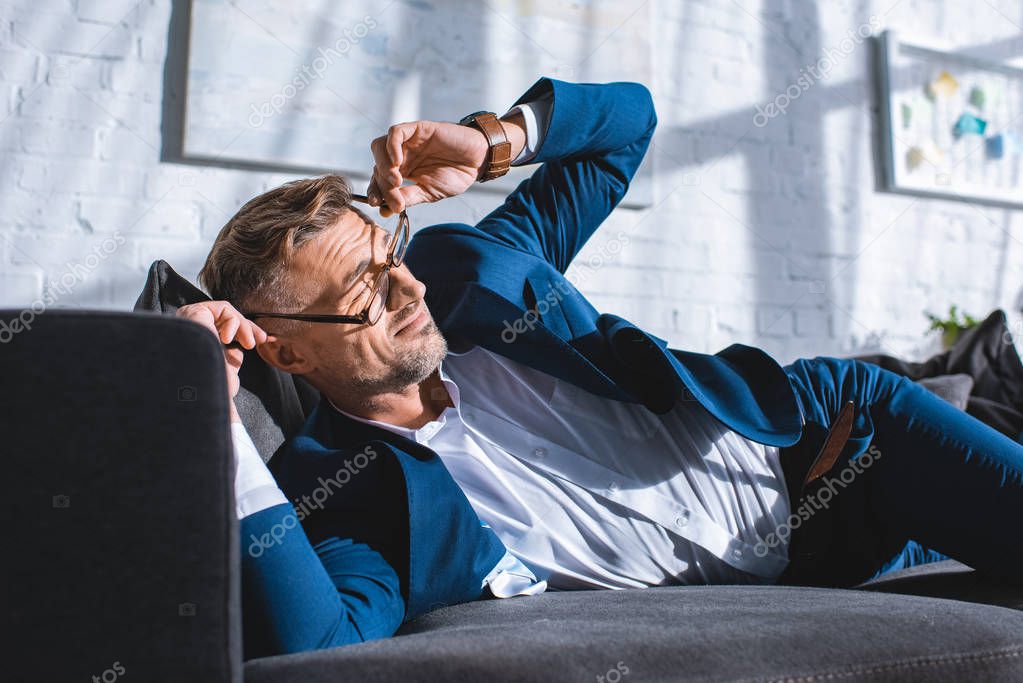 drunk businessman wearing glasses while lying on sofa 