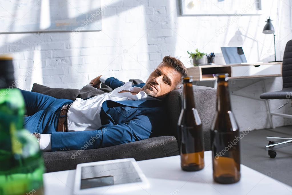 drunk businessman lying on sofa near coffee table with bottles