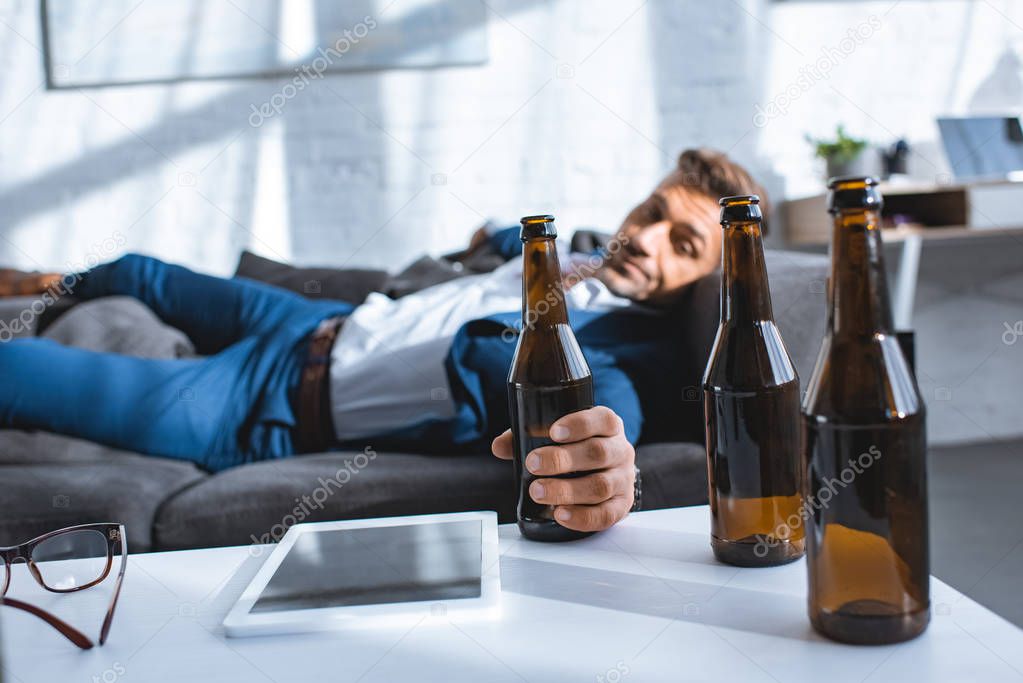 selective focus of bottle in hand of drunk businessman lying on sofa
