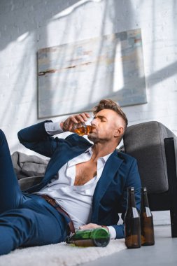 depressed businessman drinking whiskey near bottles in living room  clipart