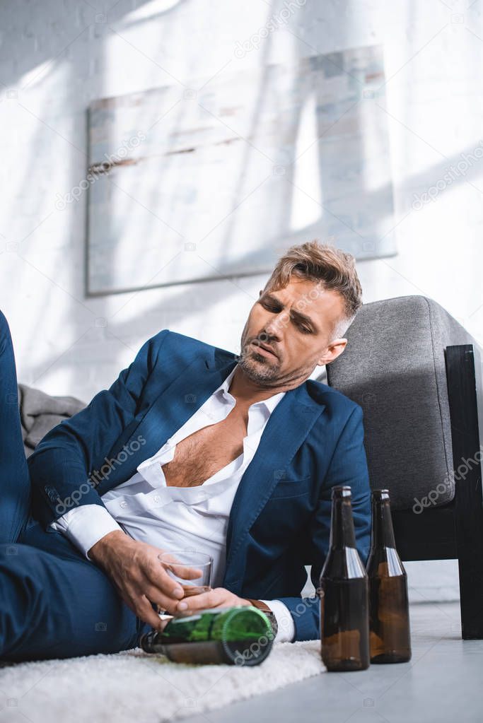 depressed and drunk businessman holding glass with alcohol drink in living room 