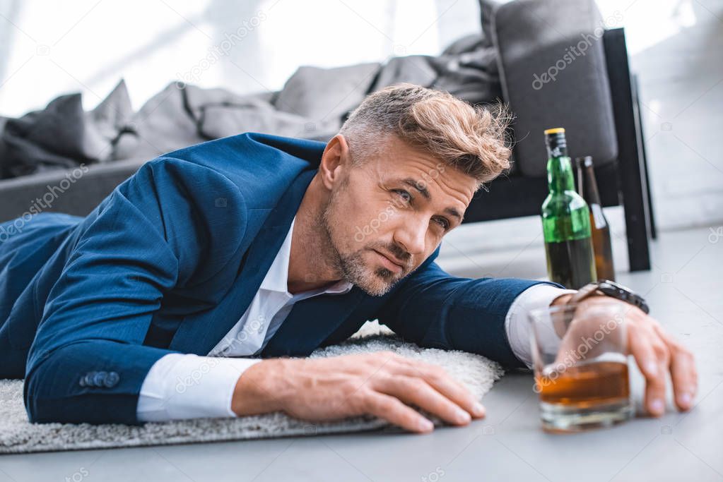 selective focus of drunk businessman lying on carpet near glass with alcohol drink