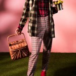 Fashionable woman in autumn checkered suit posing with basket and flowers on pink