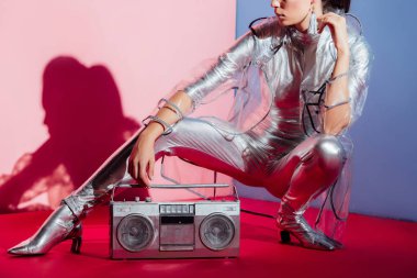 gümüş elbise ve retro boombox pembe ve mavi arka plan ile poz yağmurluk modelinin kırpılmış görünümü