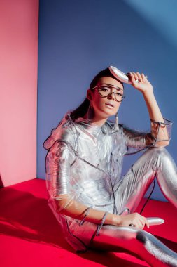 çekici moda kız metalik gömlek ve pembe ve mavi arka plan üzerinde gümüş muz ile poz yağmurluk