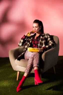 Tekli pembe bir arka plan üzerinde döner telefonuyla poz damalı elbiseli çekici kadın