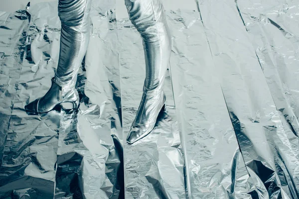 partial low section view of model posing in silver footwear on metallic background