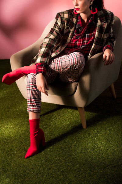 обрезанный вид стильной женщины в клетчатом костюме, позирующей в кресле
 