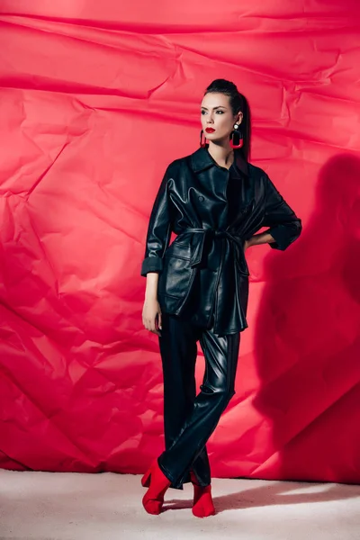 Schöne Junge Frau Posiert Schwarzem Lederanzug Auf Rotem Hintergrund — kostenloses Stockfoto