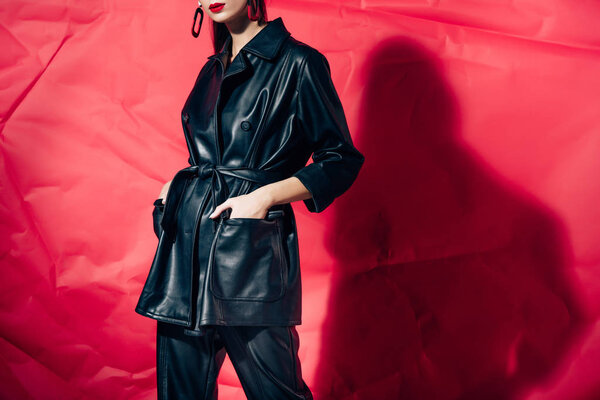 cropped view of fashionable girl posing in black leather suit on red background