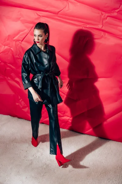 Attrayant Modèle Posant Costume Cuir Noir Sur Fond Rouge — Photo gratuite