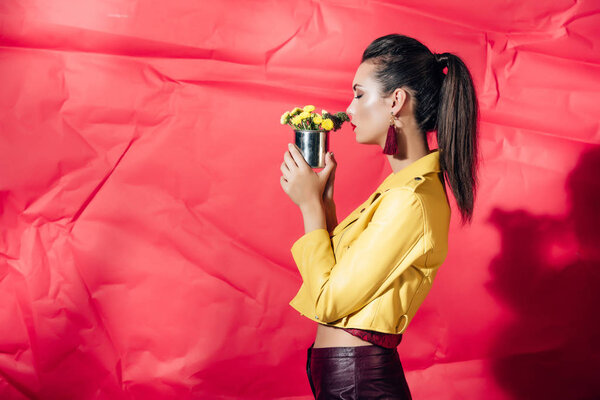 side view of fashionable girl in yellow leather jacket posing with flowers on red background
