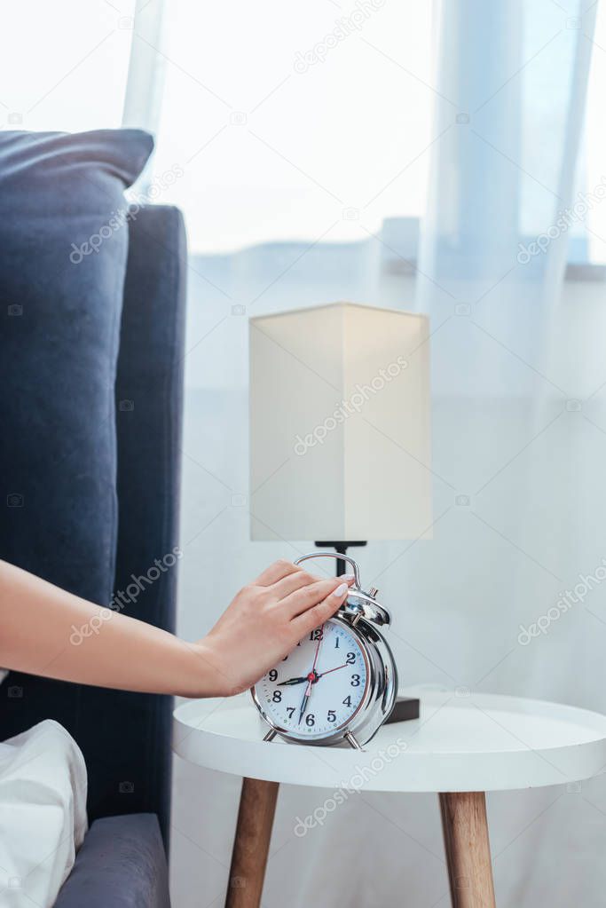 cropped image of woman turning off alarm clock in bedroom during morning time at home