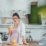 Selektywny fokus młoda kobieta trzymając kubek z soku pomarańczowego w kuchni w domu w czasie rano