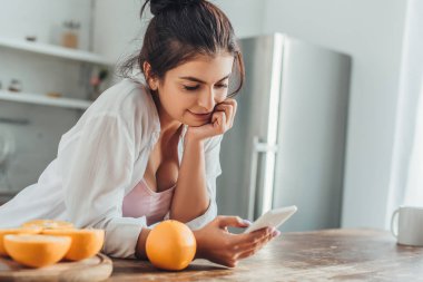 Genç kadının smartphone ile portakal evde mutfak ahşap masa saati kullanılarak seçici odak