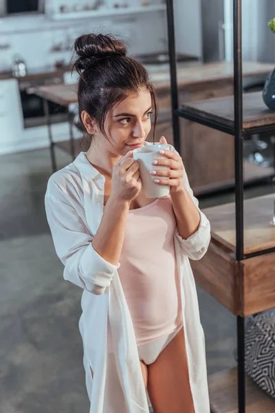 自宅で朝時間中にコーヒーを飲みながら白シャツでうれしそうな女の子 — ストック写真