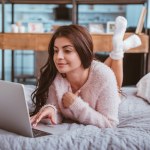 Freelancer muito feminino trabalhando no laptop enquanto deitado na cama em casa