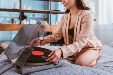 Genç kadın yatakta evde otururken vinil müzikçalar dönüm kadeh kırpılmış
