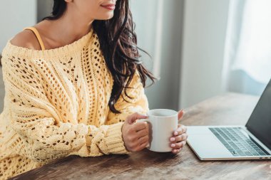 kahve fincanı tutarak ve evde mutfak içinde laptop ile tahta masada oturan kadın Freelancer kısmi görünümü