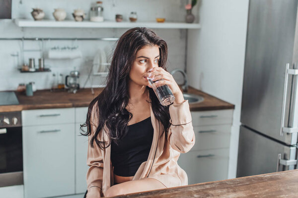 girl drinking water and sitting at wooden tabletop in kitchen at home