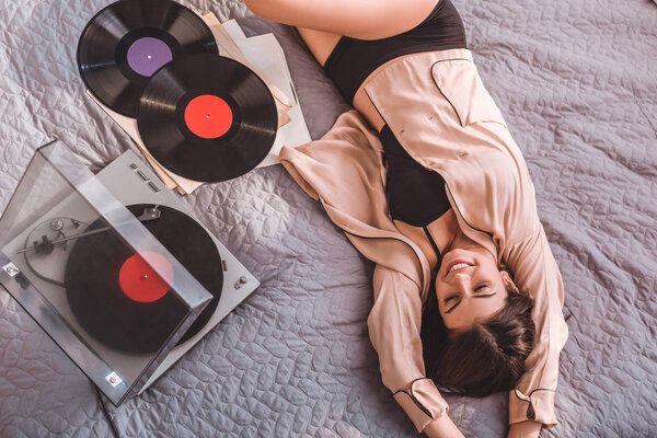 high angle view of girl laying on bed and listening vinyl audio player at home