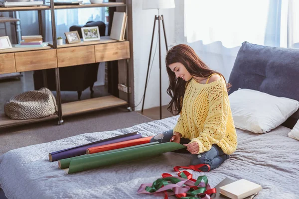 Усміхнена Дівчина Упаковує Різдвяний Подарунок Сидячи Ліжку Вдома — Безкоштовне стокове фото