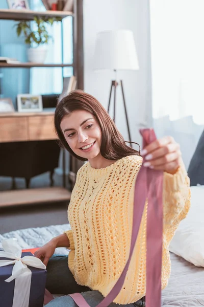 Sonriente Joven Mujer Sosteniendo Cinta Festiva Mientras Sienta Cama Casa — Foto de stock gratis