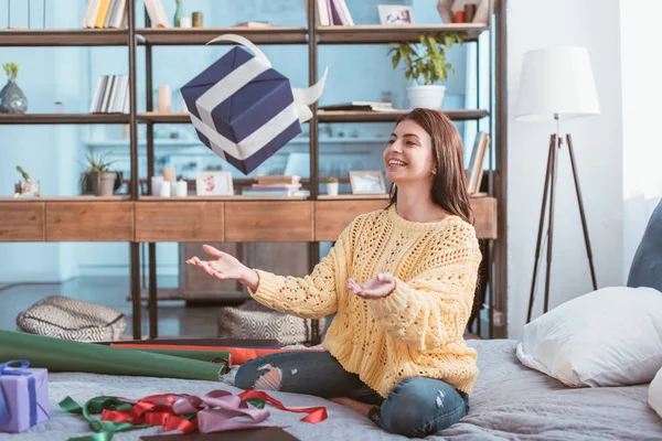 Skrattande Söt Flicka Kastar Upp Presentbox Sittande Sängen Hemma — Stockfoto