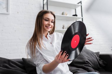 kanepede oturan ve vinil kaydı oturma odasında holding beyaz gömlek gülümseyen kız