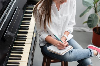 Piyano oturan ve oturma odasında müzik bestelemek defter ile kız görünümünü kırpılmış