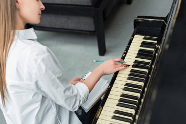 partial view of girl with notebook playing piano and composing music at home clipart