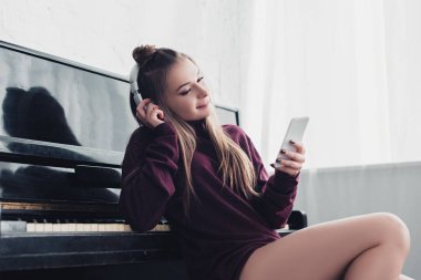 Piyano önünde oturan ve evde smartphone kullanarak kafasına kulaklık ile çekici kız
