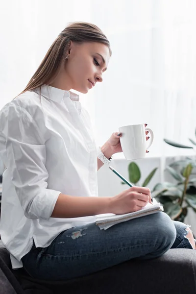 Attraktives Mädchen Weißen Hemd Sitzt Mit Kaffeetasse Und Schreibt Notizbuch — Stockfoto