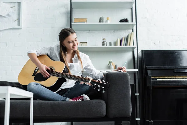 Fille Souriante Assise Sur Canapé Avec Guitare Écrire Dans Cahier — Photo