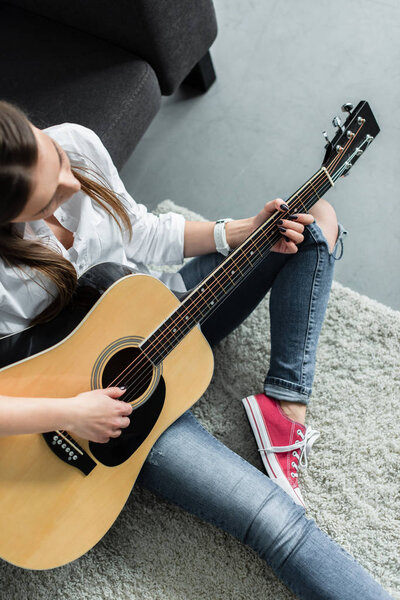 partial view of girl sitting and playing guitar in living room